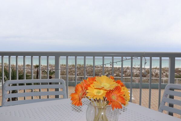 A table with a vase of flowers, white chairs, and a view of the beach. - Islander Bch Resort 2004 by AJH Rentals FREE BEACH SERVICE+TICKETS! $349/Day (Fort Walton Beach)