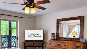 A bedroom with a bed, a dresser, a ceiling fan, a TV displaying 'Vickery Resort,' and a sliding glass door leading to an outdoor area. - Enjoy sunsets, lake activies and Sports TV pkg at this Vickery Resort Condo (Hollister)