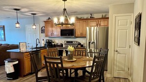A modern kitchen with wooden cabinets, a central island, and a dining table with chairs. - Enjoy sunsets, lake activies and Sports TV pkg at this Vickery Resort Condo (Hollister)