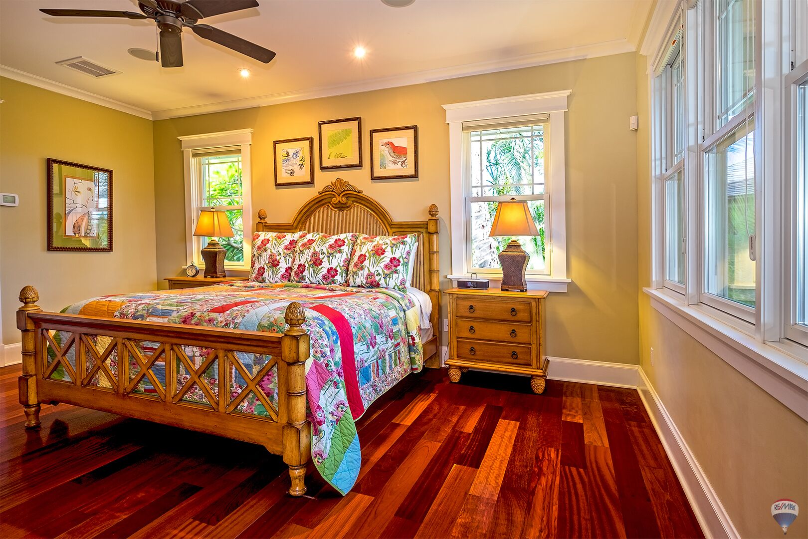 A bedroom with a wooden bed, a nightstand, a ceiling fan, and framed artwork on the wall.