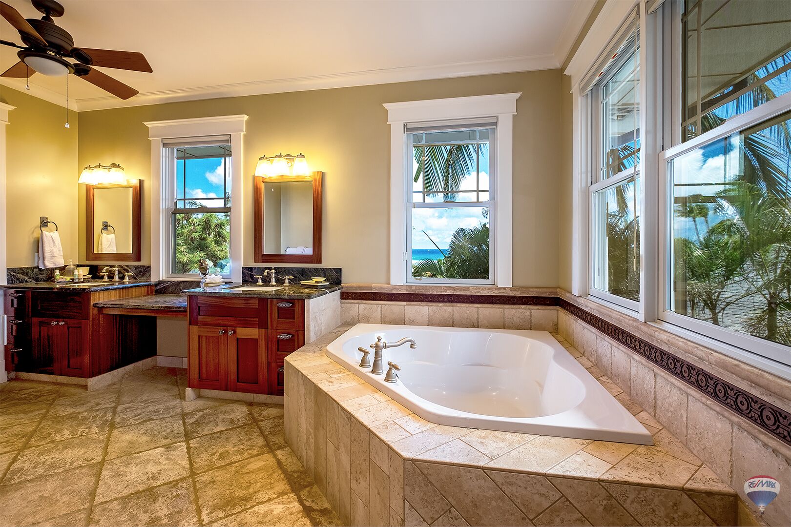 Ein Badezimmer mit einer großen Badewanne, einem Doppelwaschbecken mit Marmorplatte und einem Deckenventilator.