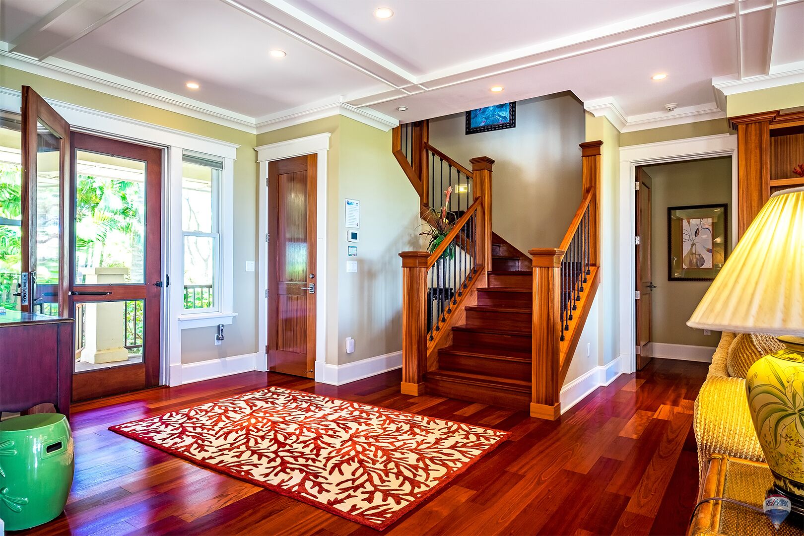 A spacious foyer with a wooden staircase, a patterned rug, and a green trash bin.