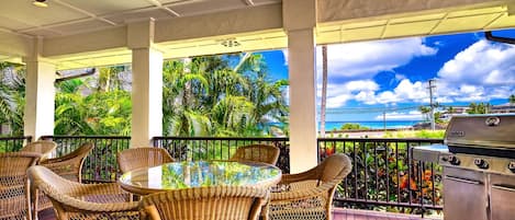 A covered outdoor area with wicker furniture, a grill, and a view of the ocean.