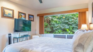 A hotel room with a large bed, a flat-screen TV, a heater, and a window with curtains. - Ground Floor Condo with Ocean and Mount Makana Views with A/C (Princeville)