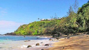 A beach with clear waters, a sandy shore, and a building on a hill. - Ground Floor Condo with Ocean and Mount Makana Views with A/C (Princeville)