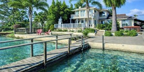 Una propiedad frente al agua con un muelle de madera, aguas cristalinas, una casa de dos pisos con balcones y palmeras.