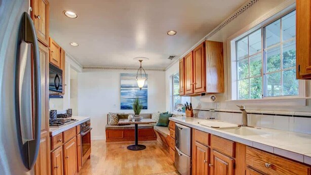 A kitchen with wooden cabinets, a stainless steel refrigerator, a sink, and a window providing natural light.