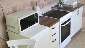 Cocina compacta con armarios blancos, microondas, estufa y pileta.