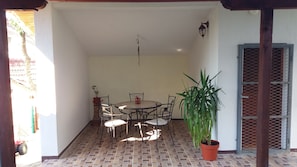 Une terrasse couverte avec une table ronde et des chaises, une plante en pot et un portail en métal.