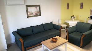 Un salon avec un canapé vert foncé, un fauteuil assorti, une table basse en bois et un tableau encadré accroché au mur.