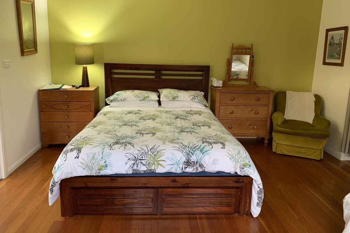 A bedroom with a wooden bed, two nightstands, a green armchair, and a mirror on the wall.