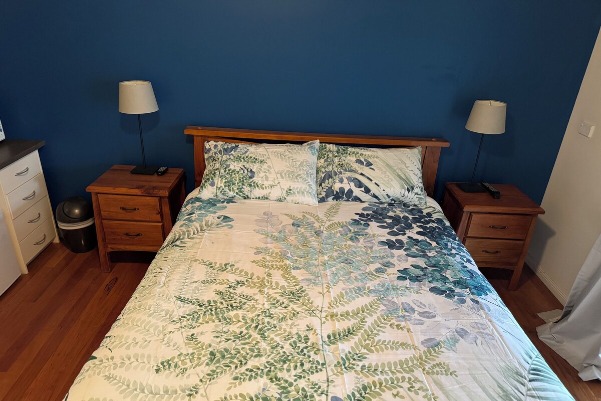 A bed with a floral bedspread, two bedside tables with lamps, a wooden dresser, and a trash can.