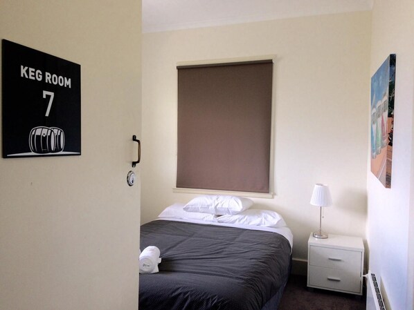 A hotel room with a bed, a nightstand, a lamp, a window with a blind, and a sign indicating it's Keg Room 7.