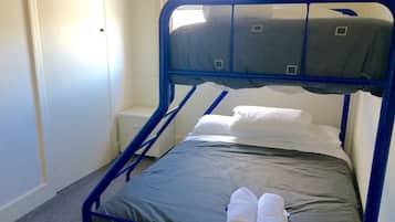 Un lit simple avec un cadre en métal, une literie grise et deux serviettes enroulées.