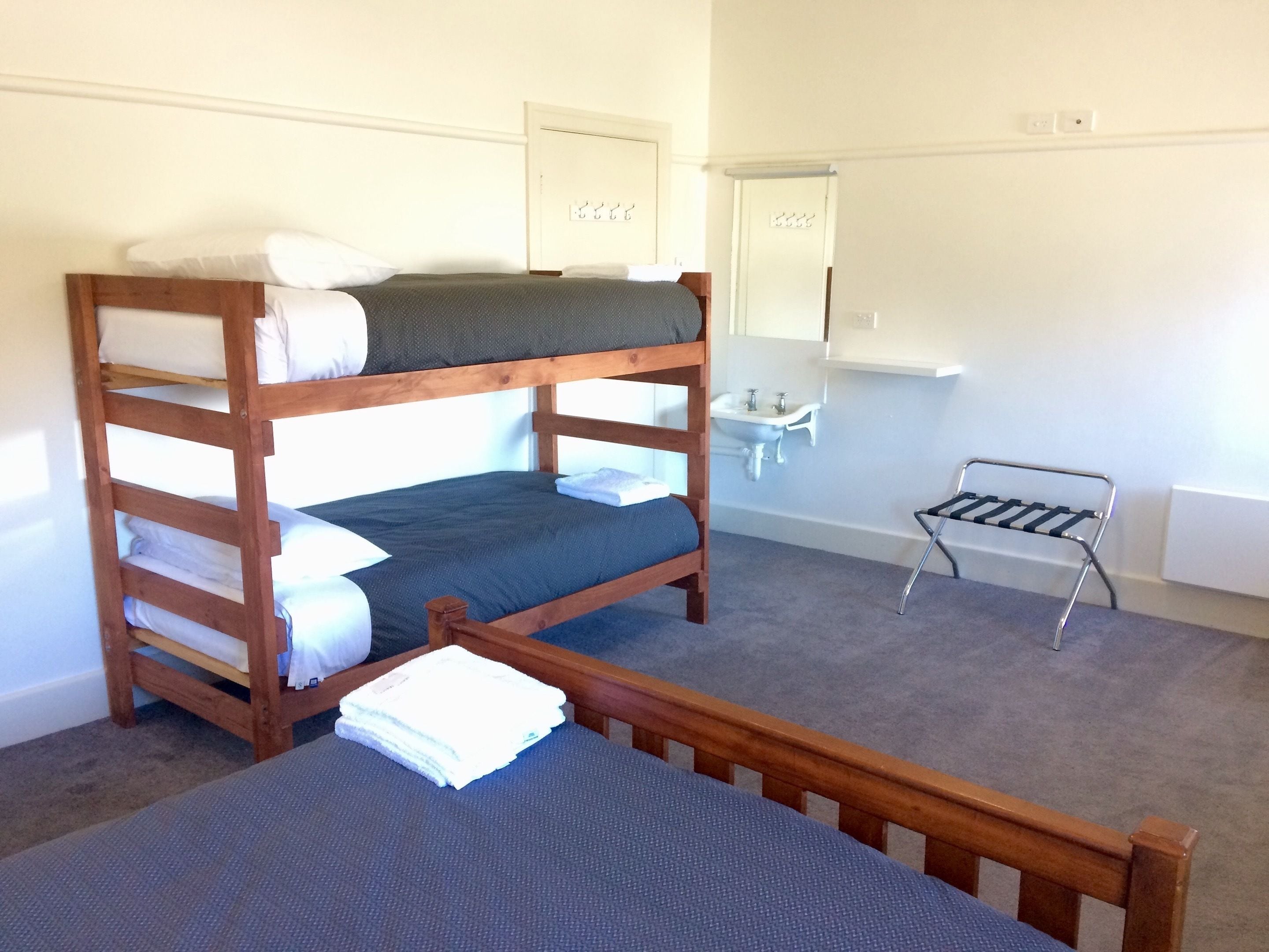 Una cama individual superpuesta con una mesita pequeña, un lavamanos y un espejo en una habitación sencilla.