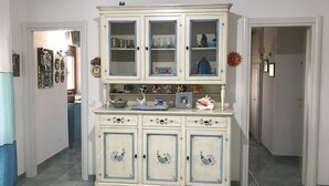 Ein weißer Schrank mit blauer Zierleiste und dekorativen Pfauenmotiven, der Glaswaren und Dekorationen beherbergt.