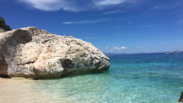 Eine felsige Küste mit klarem türkisblauem Wasser und einem Schiff in der Ferne.