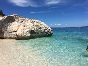 Una costa rocosa con aguas turquesas transparentes y un barco a lo lejos.