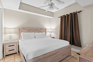 A bedroom with a wooden bed, two bedside tables with lamps, a ceiling fan, and brown curtains. - Luxury 16th Floor Condo with Breathtaking View! NEW FURNITURE! (Miramar Beach)