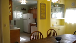 A dining area with a wooden table and chairs, a kitchen in the background, and a yellow wall. - Zion and Bryce Canyon Getaway (Glendale)