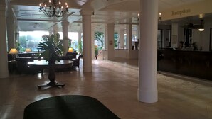 A spacious lobby with a reception desk, seating area with tables and chairs, and a chandelier.