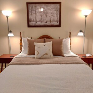 A bedroom with a large bed, two bedside lamps, a framed picture on the wall, and a nightstand with a lamp.