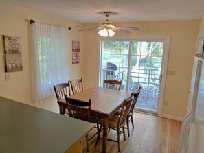 Un coin repas avec une table et des chaises en bois, un ventilateur de plafond et une vue sur l’extérieur grâce à une porte vitrée.