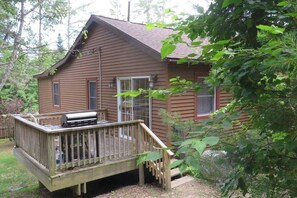 A wooden cabin with a deck, a grill, and a glass door.
