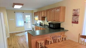 A kitchen with wooden cabinets, a microwave, and a dining area with wooden chairs.