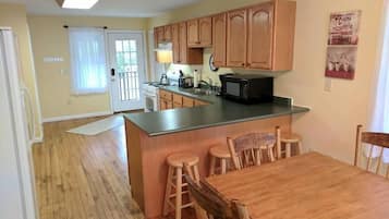 A kitchen with wooden cabinets, a microwave, and a dining area with wooden chairs.