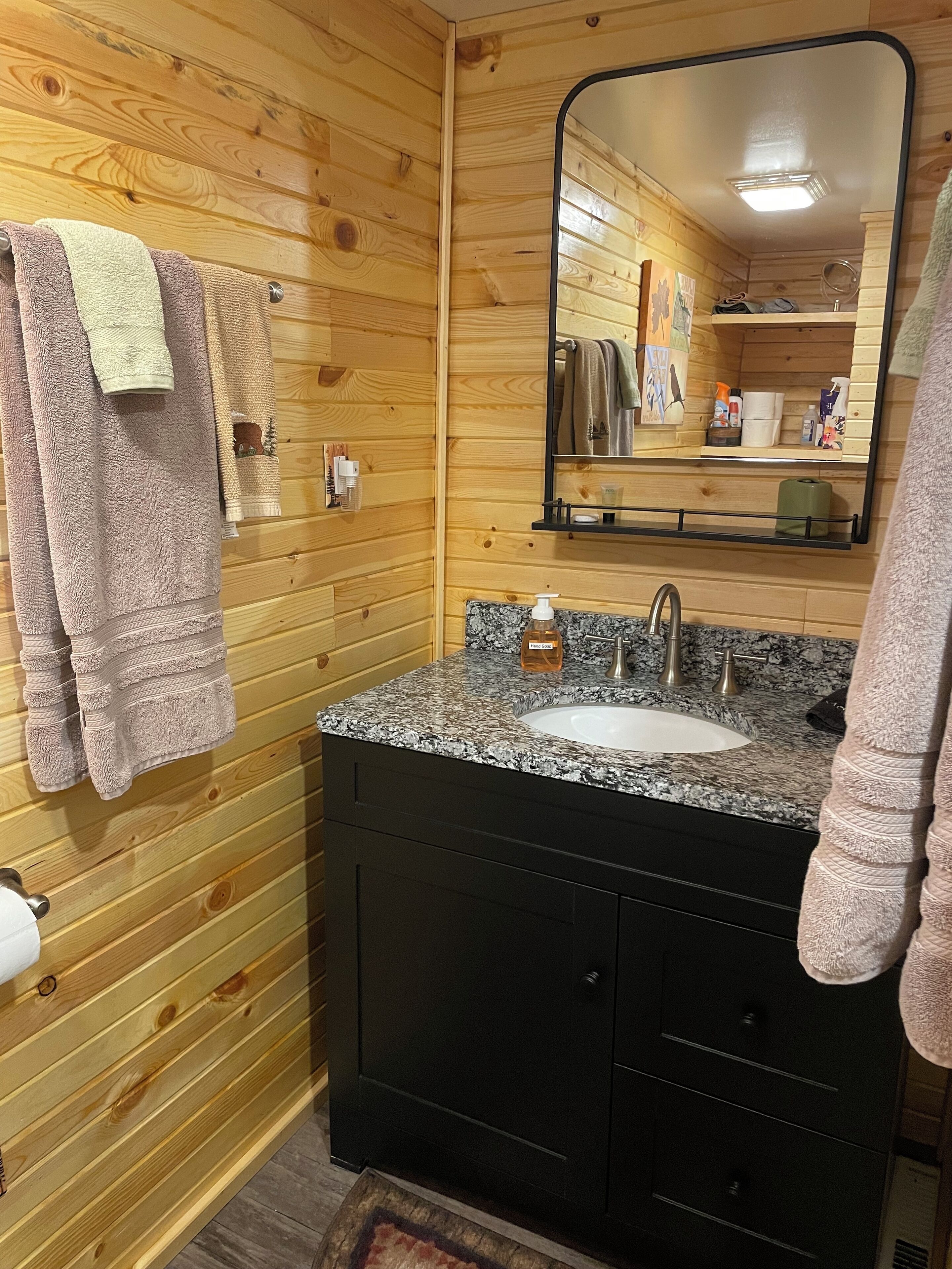 A wooden-paneled bathroom with a granite sink, a mirror, and towels hanging on the wall.