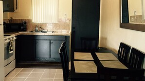 A compact kitchen with a microwave, sink, and stove, a dining area with a table and chairs, and an air conditioning unit above the door. - 2 bdrm 1 ba PRIVATE APT-close to NAVY BASE-SAVE MONEY Book now! Free internet (Sinajana)