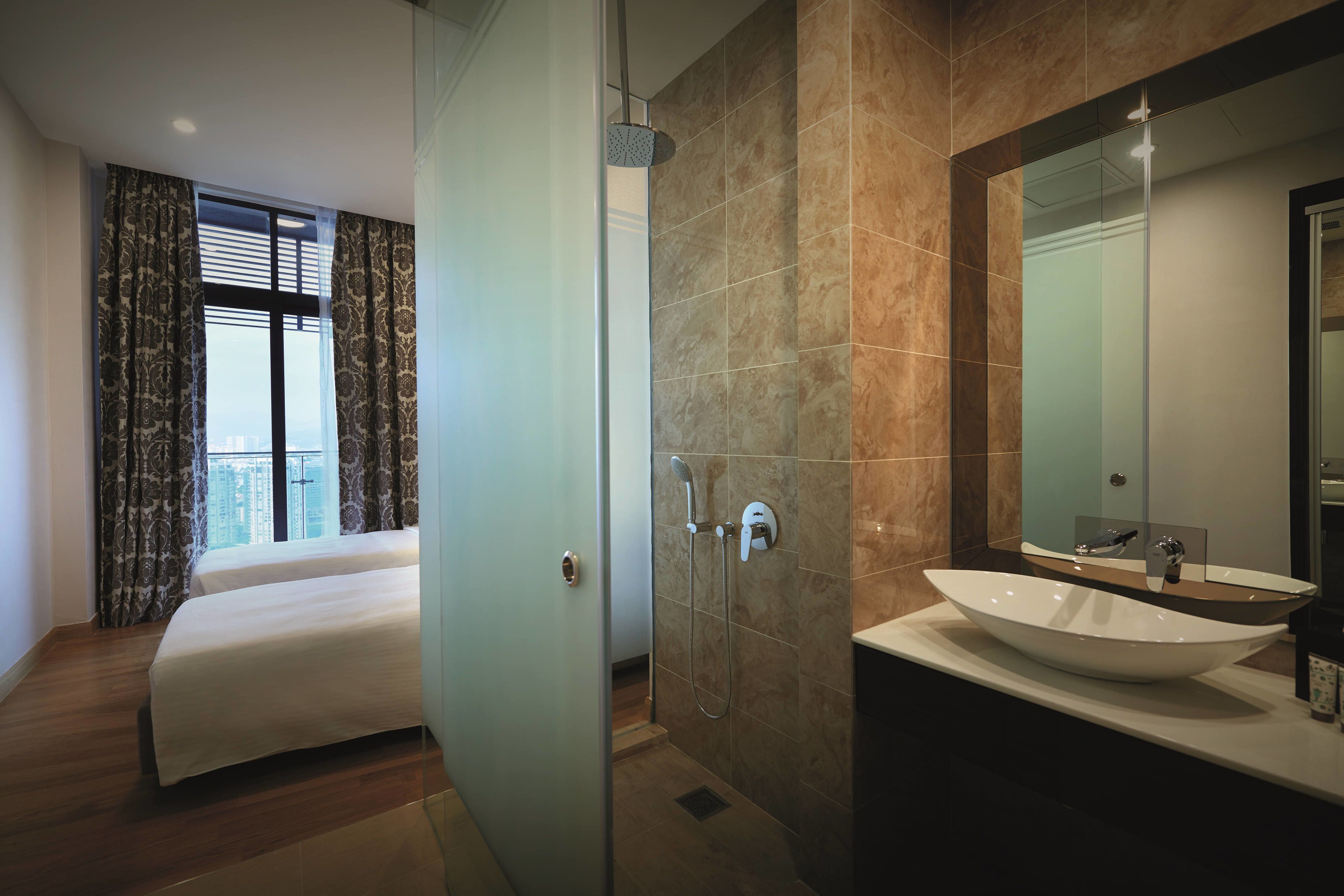 Una habitación de hotel moderna con una cama, zona de ducha y baño con un espejo grande y lavamanos.