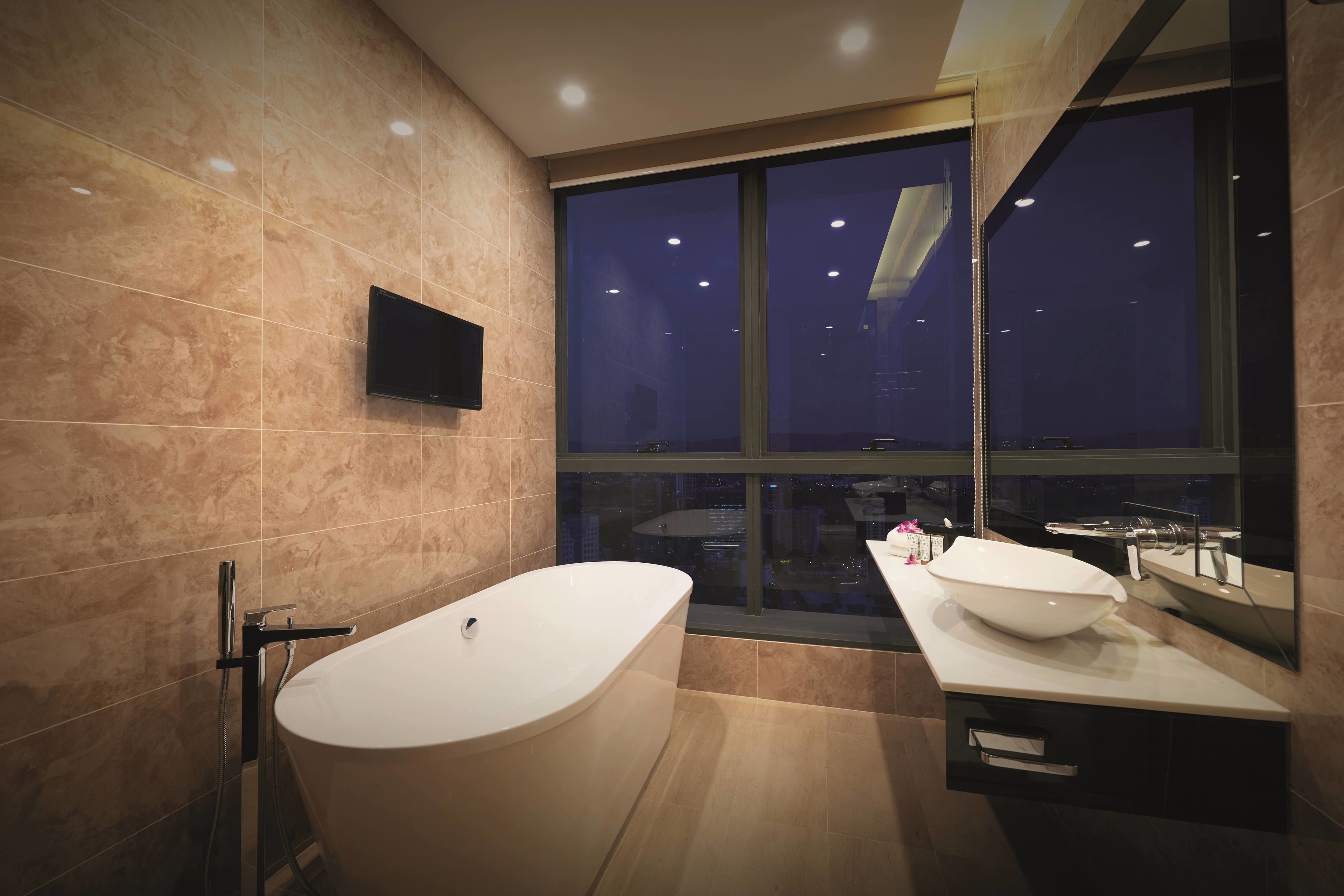 A modern bathroom with a freestanding bathtub, a double sink vanity, and a large window offering a nighttime city view.