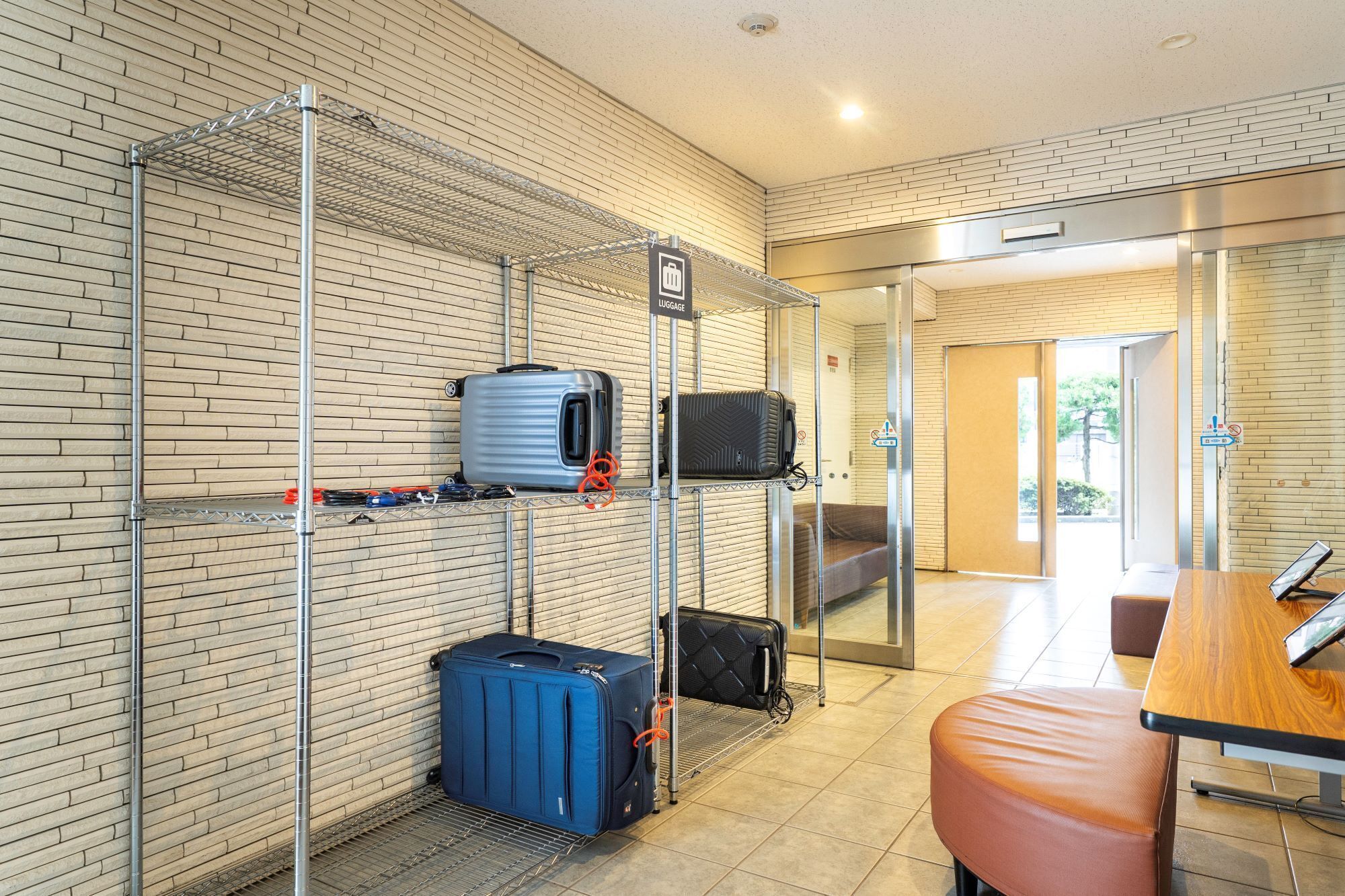 A hotel room with a luggage rack, a bed, a table, and a bathroom visible through a glass door.
