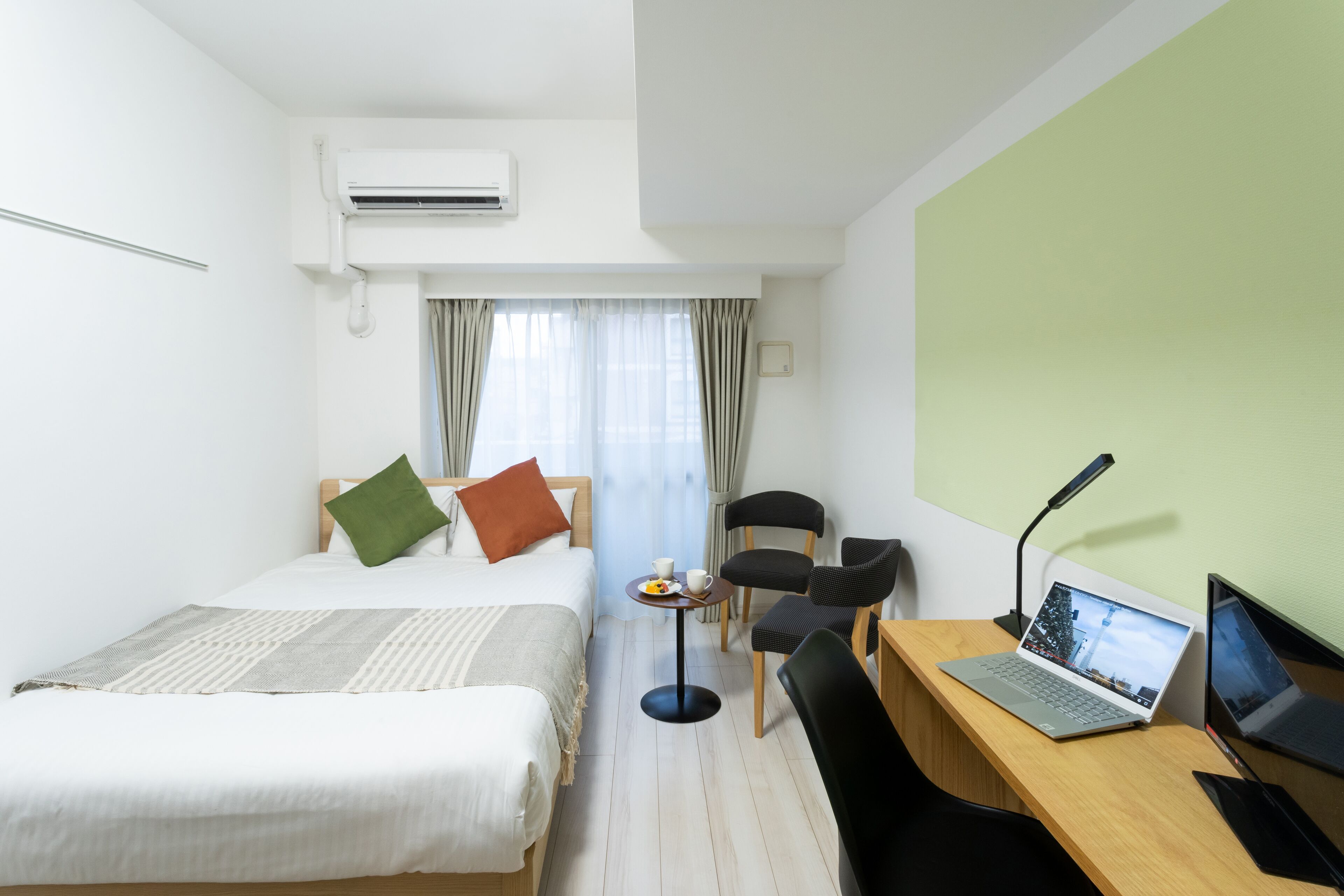 A hotel room with two beds, a desk with a laptop, a chair, and a small table with a cup and saucer.