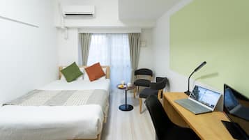 A hotel room with two beds, a desk with a laptop, a chair, and a small table with a cup and saucer.