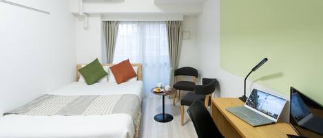 A hotel room with two beds, a desk with a laptop, a chair, and a small table with a cup and saucer.