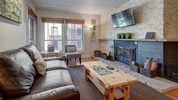 A living room with a stone fireplace, leather sofa, and a flat-screen TV mounted above it. - Paradise Meadow by Ski Colorado (Breckenridge)