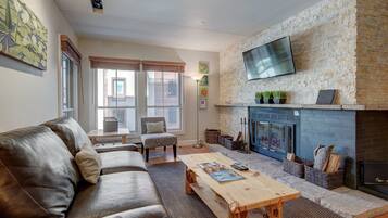 A living room with a stone fireplace, leather sofa, and a flat-screen TV mounted above it.