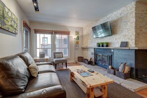 A living room with a stone fireplace, leather sofa, and a flat-screen TV mounted above it. - Paradise Meadow by Ski Colorado (Breckenridge)