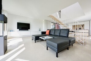 Ein modernes Wohnzimmer mit einer Eckcouch, einem Flachbildfernseher und einer Treppe mit weißer Geländer.