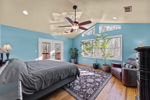 A bedroom with a bed, a ceiling fan, a window, and a potted plant.