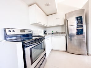 Features a stove, microwave, and refrigerator with white cabinetry and a tiled backsplash.