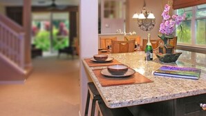 Una cucina con un piano di lavoro in granito, sgabelli di legno, un tavolo da pranzo e un vaso con fiori viola.