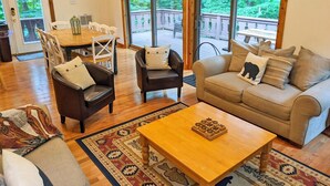 A cozy living room with a wooden coffee table, a beige sofa with patterned cushions, and a dining area with a wooden table and chairs. - Classic VT Ski Chalet - Walkable to Okemo Ski Lift w/Fit Pit & Pool Table (Ludlow)