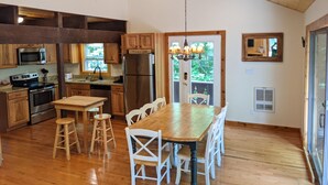 A spacious kitchen with wooden cabinets, stainless steel appliances, and a large dining table with white chairs. - Classic VT Ski Chalet - Walkable to Okemo Ski Lift w/Fit Pit & Pool Table (Ludlow)