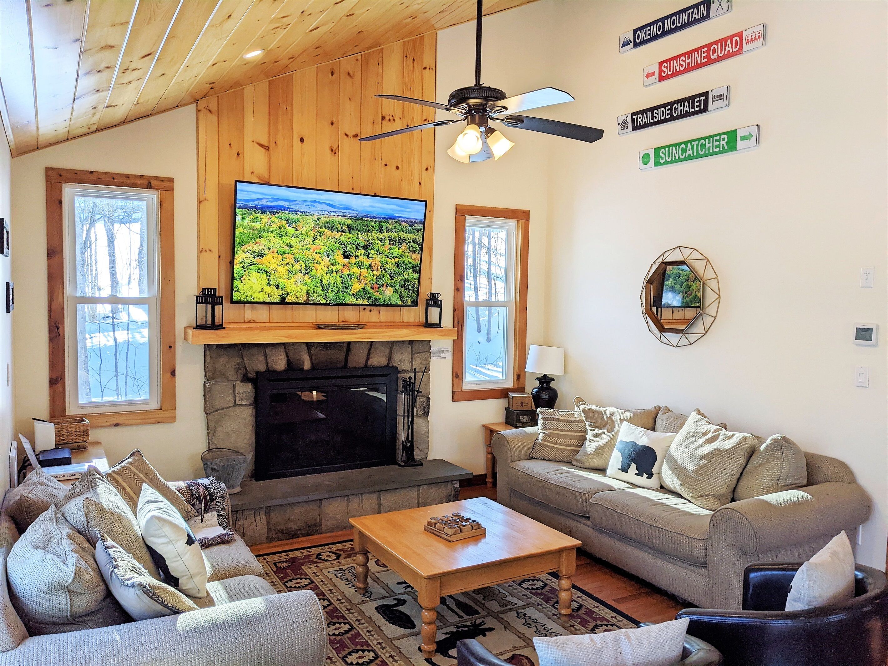 A cozy living room with a fireplace, a television mounted on the wall, and a ceiling fan.