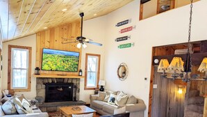 A cozy living room with a fireplace, comfortable seating, a television, and wooden accents. - Classic VT Ski Chalet - Walkable to Okemo Ski Lift w/Fit Pit & Pool Table (Ludlow)