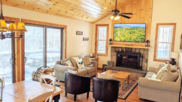 A cozy living room with a fireplace, wooden ceiling, and a large TV screen. - Classic VT Ski Chalet - Walkable to Okemo Ski Lift w/Fit Pit & Pool Table (Ludlow)